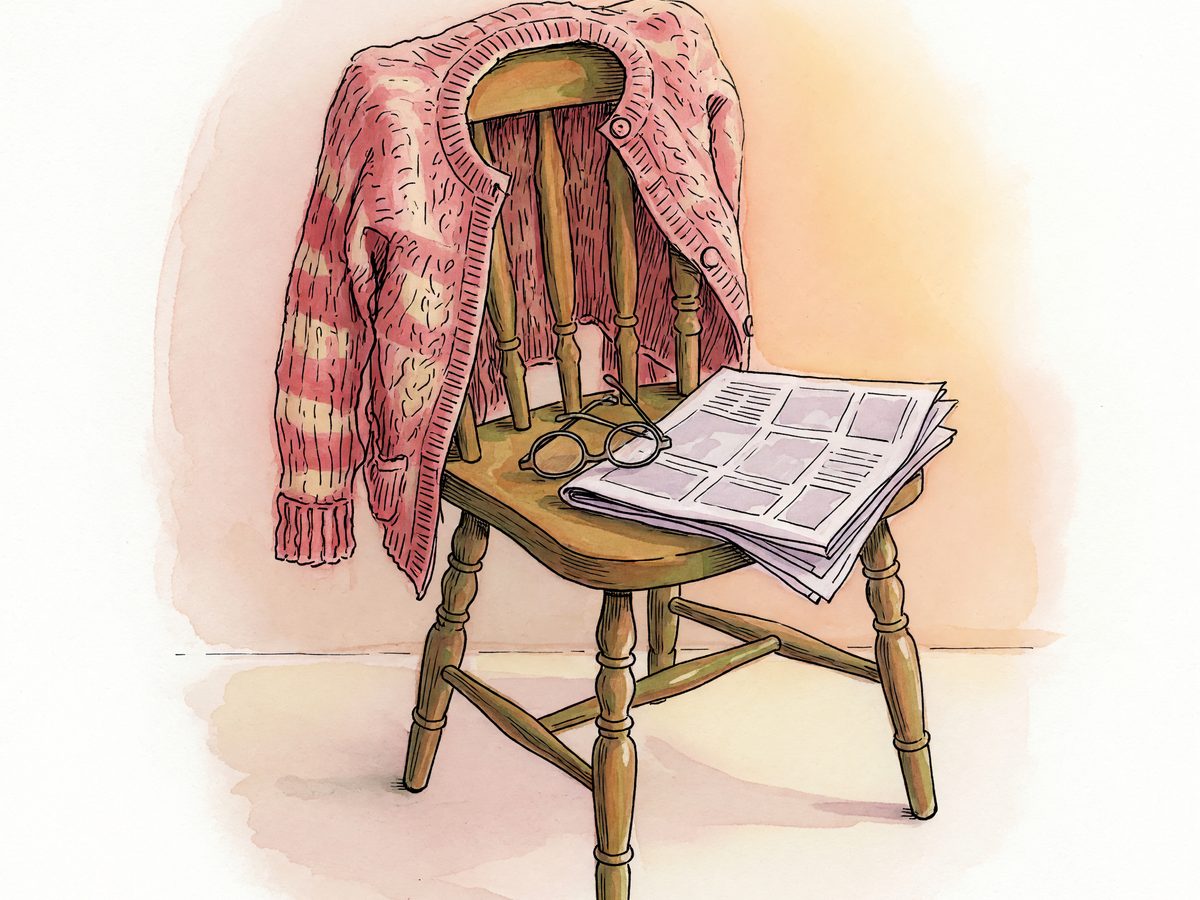 A knitted cardigan on a chair with reading glasses resting nearby